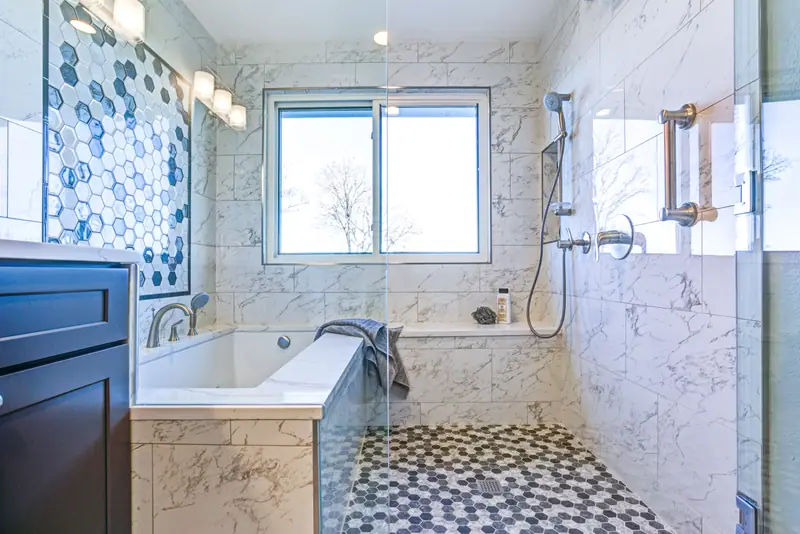 Walk-in shower with blue hexagon accent tile, marble walls and built-in soaking tub