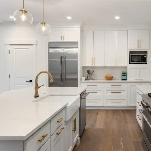 White shaker kitchen with brass faucet, quartz counters and paneled refrigerator wall