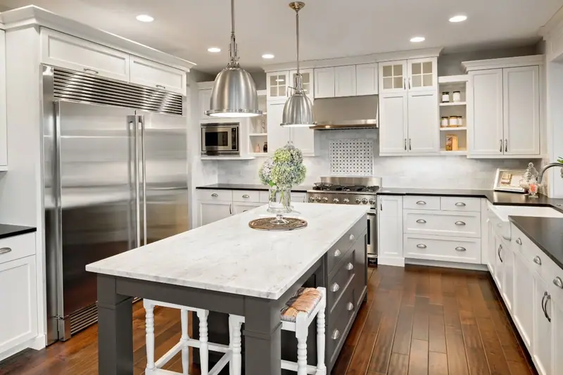 White kitchen with gray island, marble countertops and stainless steel appliances
