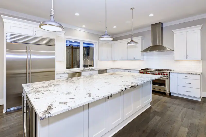 Remodeled white shaker kitchen with oversized granite island, stainless range hood and wide-plank flooring